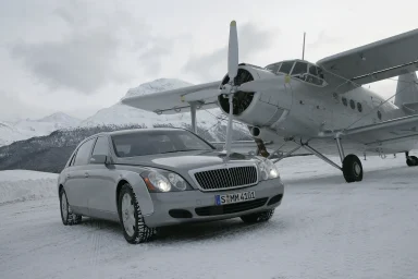 Silberner Maybach 57 steht in einer verschneiten Berglandschaft vor einem historischen Propellerflugzeug.