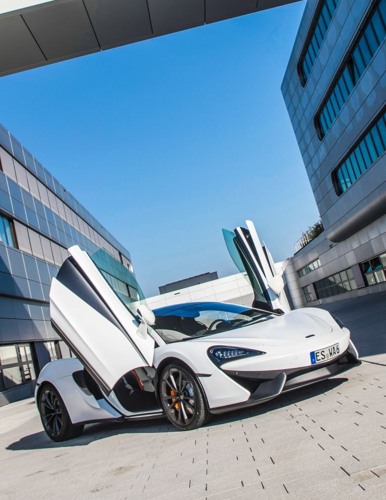 McLaren 570S mit geöffneten Flügeltüren – Automobilfotografie von Dieter Rebmann Weißer McLaren 570S mit geöffneten Flügeltüren vor moderner Architektur in dynamischer Perspektive.
