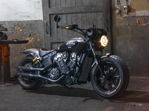 Indian Scout Bobber vor historischer Industriehalle mit eingeschaltetem Scheinwerfer und markantem V2-Motor.