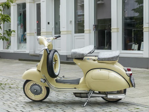 Cremefarbene Vespa VNA1T Baujahr 1958 mit Doppelsattel und Reserverad vor historischer Fassade.