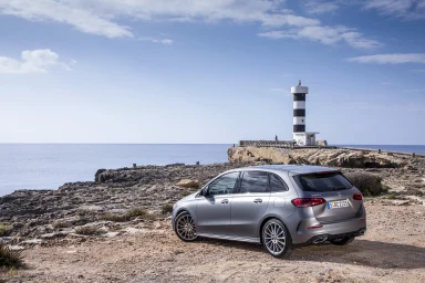 Silberne Mercedes-Benz B-Klasse an einer felsigen Küste mit schwarz-weißem Leuchtturm und Blick auf das Meer.