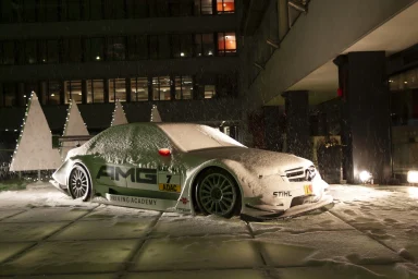 Mercedes-Benz C-Klasse DTM Rennwagen der AMG Driving Academy, nachts im Schneefall von einer frischen Schneedecke bedeckt.