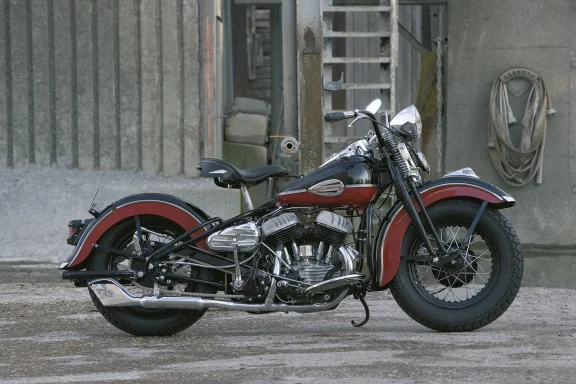 Harley-Davidson Flathead Vintage-Bobber in Schwarz und Dunkelrot vor historischer Industriekulisse, professionell fotografiert.