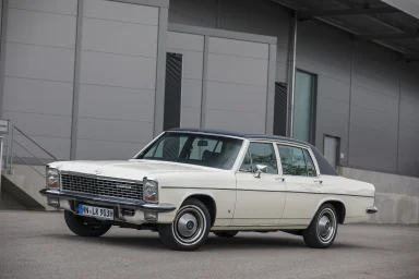 Weißer Oldtimer mit Chromdetails, vor modernen Gebäuden geparkt.
