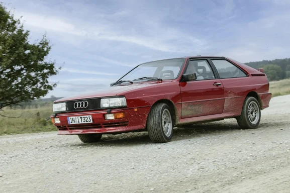 Roter Audi Urquattro in schneller Fahrt auf einer Schotterstraße.
