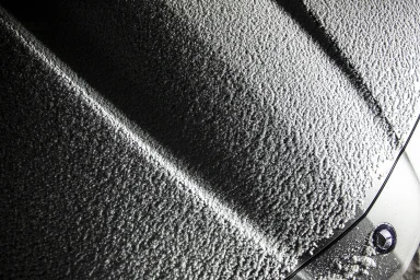 Nahaufnahme von Froststrukturen auf der Motorhaube eines Mercedes-Benz SL mit abstrakten Licht- und Schattenverläufen.