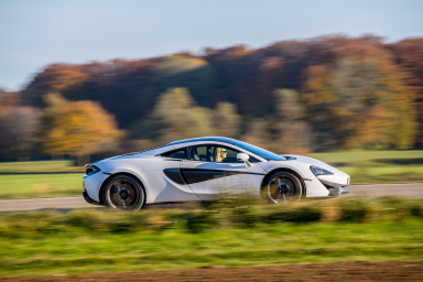 Weißer McLaren 570S in Seitenansicht auf einer Landstraße vor herbstlicher Landschaft.