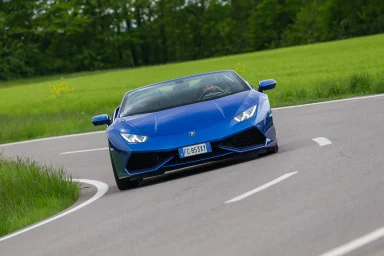 Blauer Lamborghini Huracán Spyder in dynamischer Kurvenfahrt auf einer Landstraße.