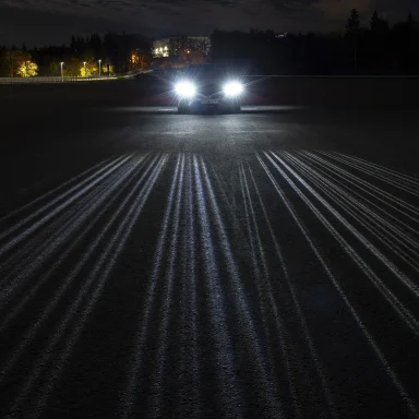 Heller Fahrzeugscheinwerfer in der Nacht mit feinen Lichtspuren auf verschneiter Fahrbahn.