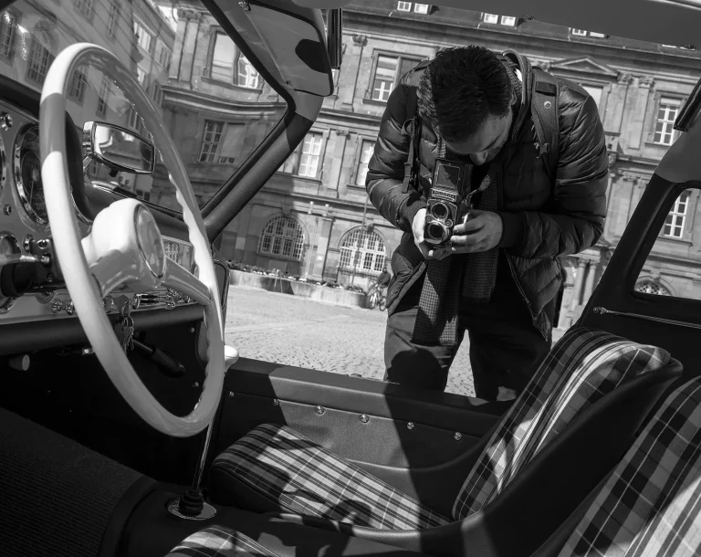 Fotograf mit analoger Kamera fotografiert den Innenraum eines Mercedes-Benz 300 SL Flügeltürers in Schwarz-Weiß.