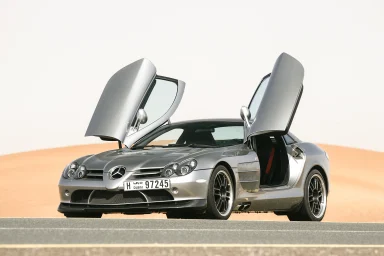 Silberner Mercedes SLR McLaren Edition 722 mit offenen Flügeltüren auf einer Straße in der Wüste.