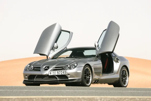 Silberner Mercedes SLR McLaren Edition 722 mit offenen Flügeltüren auf einer Straße in der Wüste.