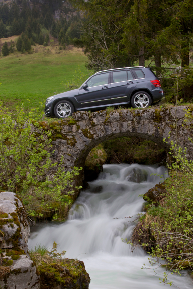 Ein anthrazitgrauer SUV steht auf einer Steinstraßenbrücke über einem fließenden Bach.