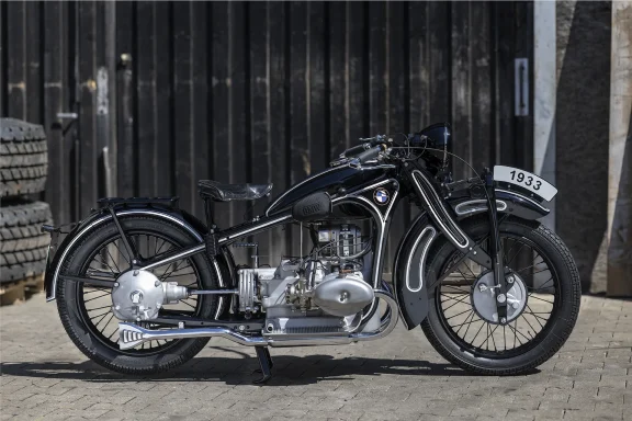 BMW R 16 Serie IV von 1933 in schwarzer Lackierung vor dunklem Industriehintergrund.