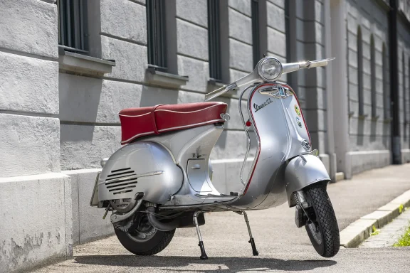 Silberne Vespa GS/3 Baujahr 1961 mit roter Sitzbank vor historischer Architektur.