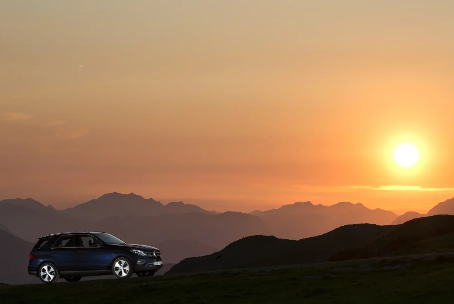 Ein Auto steht silhouettenhaft vor einem Sonnenuntergang über den Bergen.