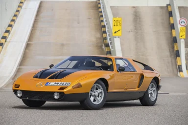 Ein orangefarbener Sportwagen Mercedes-Benz C111 II mit schwarzem Streifen. Hintergrund mit einer steilen Auffahrt