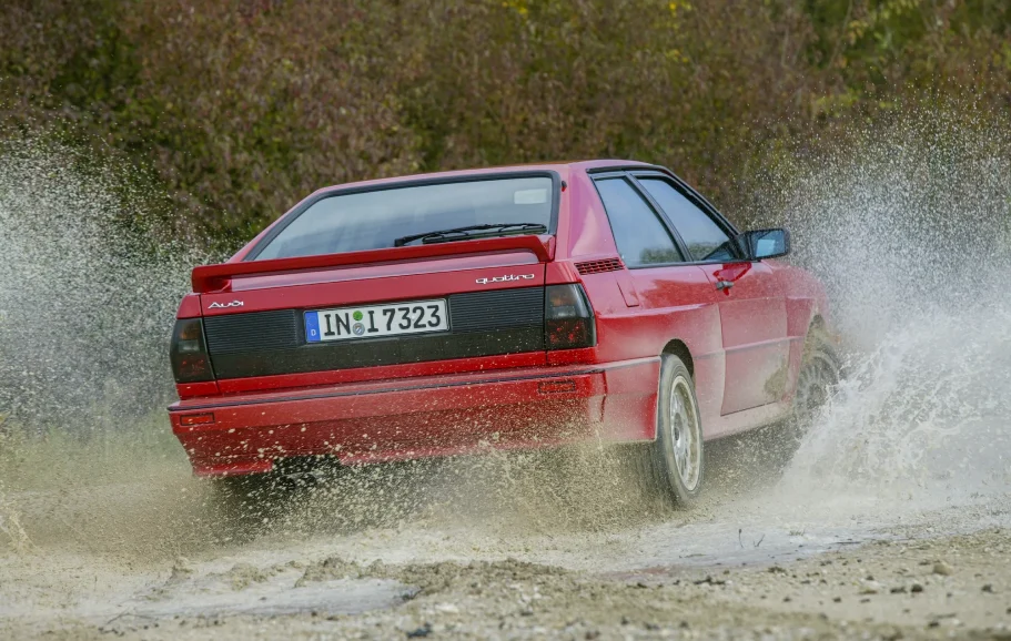 Audi Ur-quattro in voller Fahrt Roter Audi Ur-quattro durchquert eine Wasserpassage und erzeugt eine hohe Gischt.