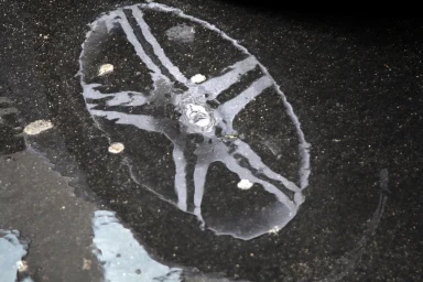 Abstrakte Spiegelung einer Mercedes Felge in einer Pfütze auf nassem Asphalt.
