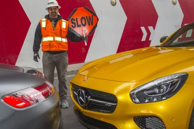 Baustellenmitarbeiter mit „SLOW“-Schild zwischen zwei Mercedes-AMG Sportwagen