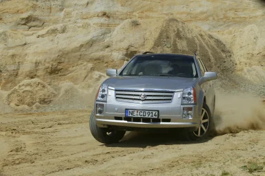 Silberner Cadillac SRX bei einer dynamischen Fahrt auf sandigem Untergrund mit aufgewirbeltem Staub.
