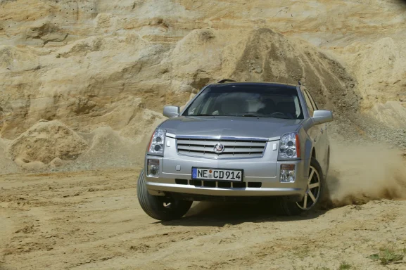 Silberner Cadillac SRX bei einer dynamischen Fahrt auf sandigem Untergrund mit aufgewirbeltem Staub.