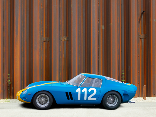 Blauer Sportwagen mit der Nummer 112 vor einer rostigen Metallwand.
