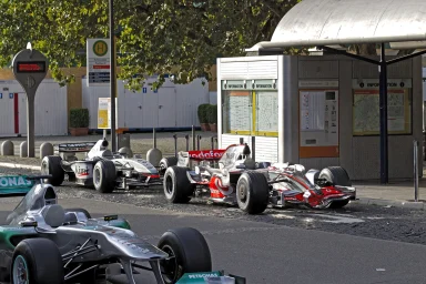 Drei Formel-1-Rennwagen an einer Bushaltestelle am Schlossplatz in Stuttgart.