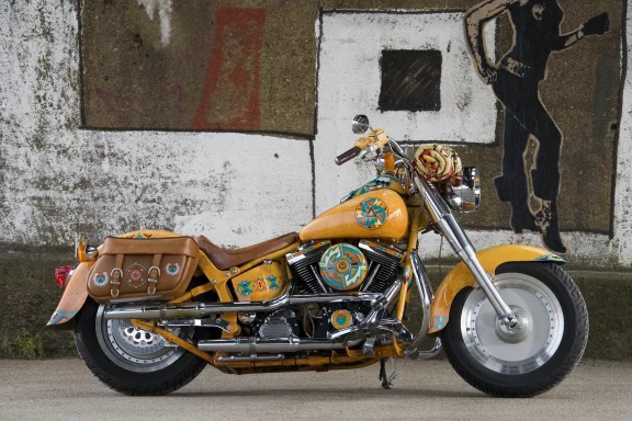 Harley-Davidson Fat Boy Custom mit Indian-Style-Lackierung und Ledertaschen vor einer Betonwand.
