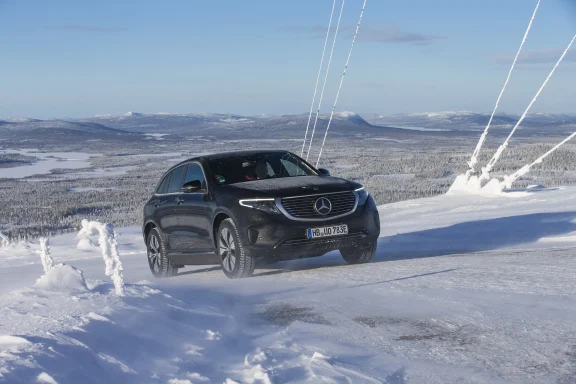 Schwarzer Mercedes-Benz EQC 400 4MATIC auf verschneiter Bergstraße mit winterlicher Landschaft und schneebedeckten Bergen im Hintergrund.