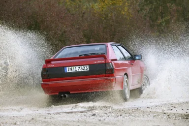 Roter Audi quattro bei dynamischer Fahrt durch eine Wasserpassage mit hoher Gischt.