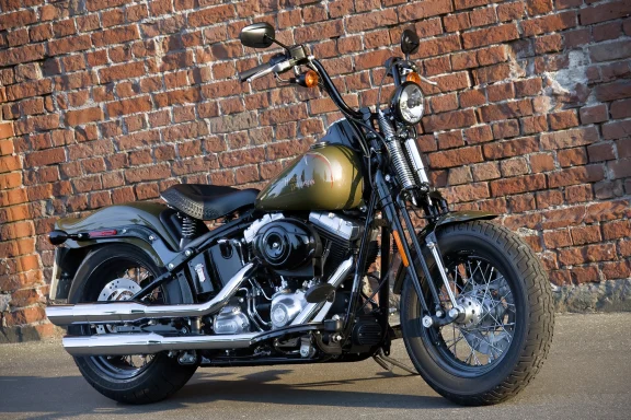 Harley-Davidson Softail Springer in Olivgrün mit Springer-Gabel vor einer Backsteinmauer.
