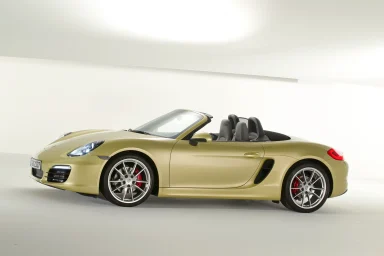 Goldfarbener Porsche Boxter in Seitenansicht auf weißem Studiohintergrund mit geöffnetem Verdeck.
