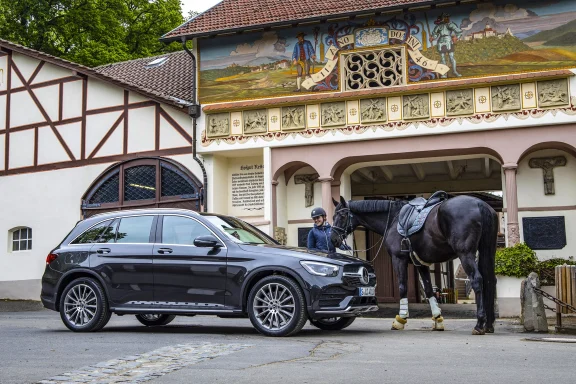 Schwarzer Mercedes-Benz GLC AMG Line vor einem historischen Hofgebäude mit bemalter Fassade. Daneben steht ein gesatteltes schwarzes Pferd.