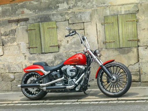 Harley-Davidson Softail Breakout (FXSB) in Rot mit Apehanger-Lenker und Custom-Rädern vor einer historischen Natursteinmauer.