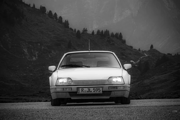 Frontansicht eines Citroën CX 25 GTI Turbo vor einer alpinen Berglandschaft in Schwarzweiß.