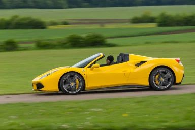 Gelber Ferrari 488 Spider in Seitenansicht auf einer Landstraße vor grüner Landschaft.