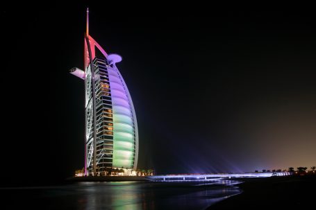 Burj Al Arab in Dubai bei Nacht, farbig beleuchtet am Meer.