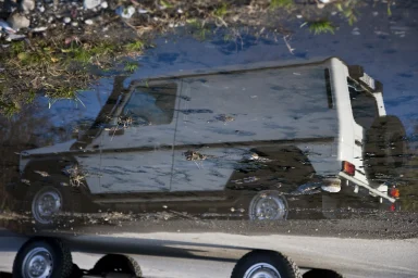Spiegelung eines Mercedes-Benz G-Modells in einer Pfütze mit abstrakten Reflexionen und natürlichen Strukturen.