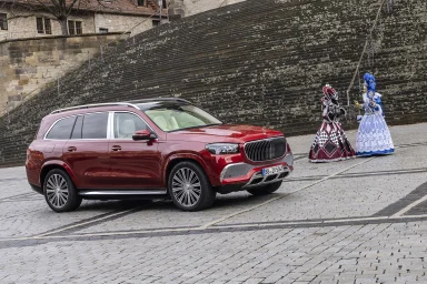 Roter Mercedes-Maybach GLS 600 auf einem historischen Platz vor großer Steintreppe, daneben zwei Personen in venezianischen Kostümen.