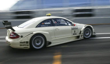 Weißer Mercedes-Benz CLK DTM AMG Renntaxi mit Startnummer 1 bei schneller Fahrt auf nasser Rennstrecke mit Bewegungsunschärfe.