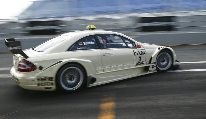 Weißer Mercedes-Benz CLK DTM AMG Renntaxi mit Startnummer 1 bei schneller Fahrt auf nasser Rennstrecke mit Bewegungsunschärfe.