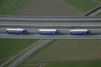 Drei Lkw der Spedition Wiedmann & Winz fahren in Kolonne auf einer Autobahnbrücke aufgenommen aus der Vogelperspektive.