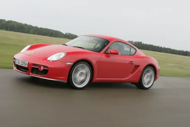Roter Porsche Cayman S in dynamischer Fahrt auf einer Landstraße.