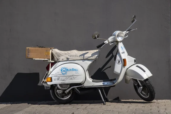 Weiße Vespa PX 200 E Lusso Baujahr 1982 mit Gepäckbox und historischem Dekor.
