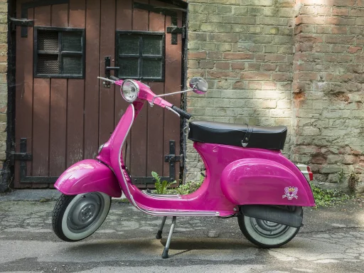 Vespa 50 L Baujahr 1968 in Shocking Pink vor historischer Backsteinfassade.
