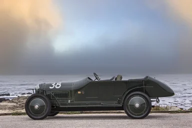 Klassischer Rennwagen in dunklem Grünton am Strand, mit der Nummer 36.