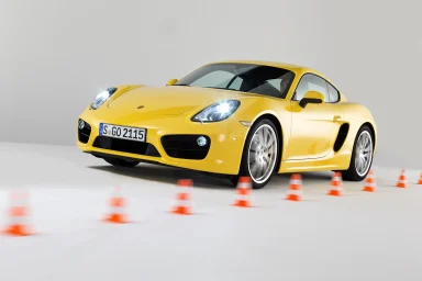 Gelber Porsche Cayman fährt zwischen Pilonen auf weißem Hintergrund.
