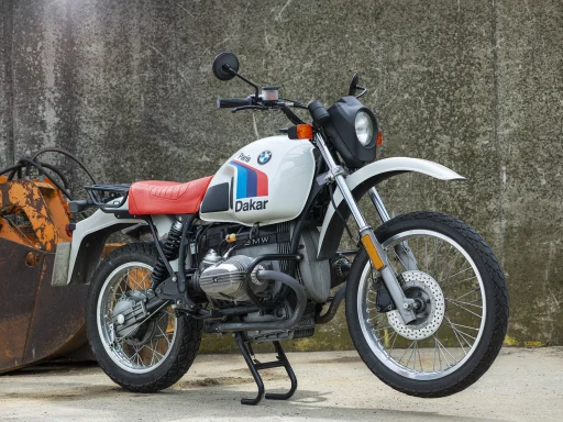 BMW R100 GS Paris-Dakar mit roter Sitzbank und Paris-Dakar-Lackierung vor einer Betonwand.
