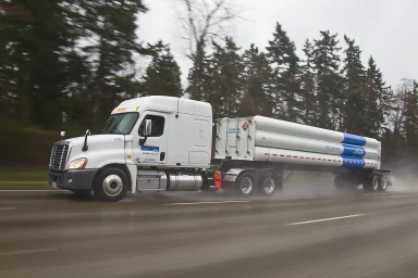 Weißer Freightliner Sattelzug mit Wasserstoffauflieger fährt bei Regen auf einer Autobahn.